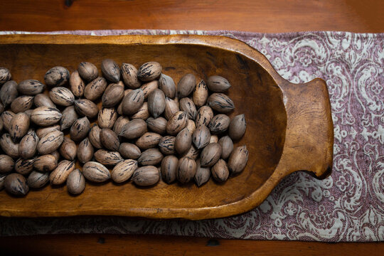 Raw in shell whole Pecan nuts in a wooden bowl on a wood table