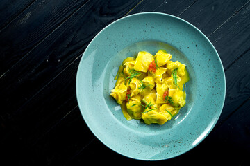 Homemade and mouth-watering ravioli with salmon and caviar, served with custard sauce in a blue plate on a dark wood background. Dish of italian cuisine