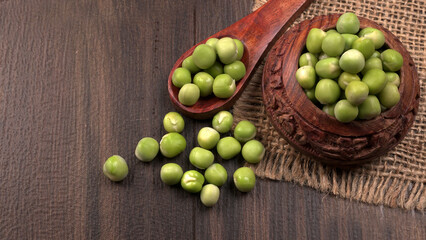 Fresh green peas in wooden bowl on wooden background.