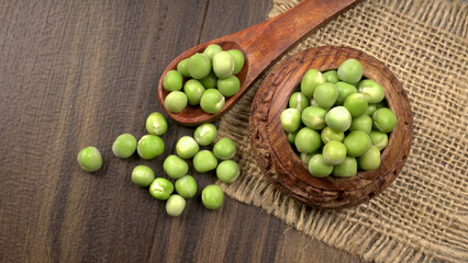 Fresh green peas in wooden bowl on wooden background.