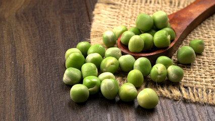 Fresh green peas in spoon on wooden background.