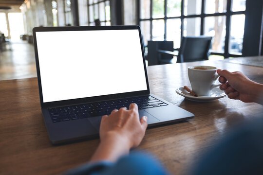 Mockup image of a woman using and touching on laptop touchpad with blank white desktop screen while drinking coffee
