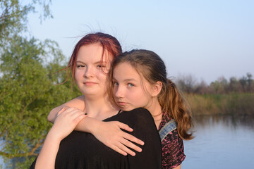 Two teenage sisters hug on the river bank