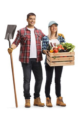 Full length portrait of a male farmer holding a shovel and a female farmer holding a crate with vegetables - obrazy, fototapety, plakaty