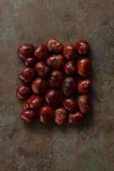 Ripe chestnuts on dark rustic background, close up. Raw Chestnuts for Christmas. Fresh sweet chestnuts lined in a rectangular shape.  Food background.