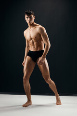 Fototapeta na wymiar athletic men with a pumped-up muscular body in black shorts posing against a dark background