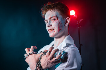 Portrait of a maniac with blood on his face and chain in his hands against a background of red and...