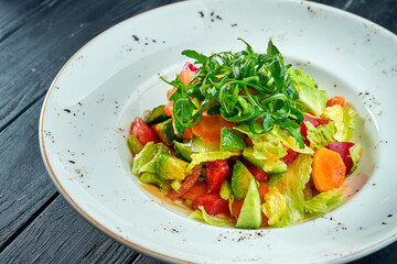 Diet and vegetarian salad of mixed vegetables and lettuce with peanut sauce, served in a white plate on a black wood background