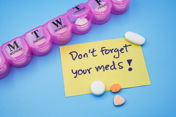 Yellow sticky note with wording Don't forget your meds with medicines and pills organizer box or...