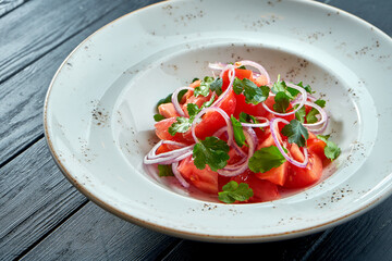 Salad with tomatoes and onions, olive oil in a white plate on a black background.