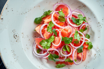 Salad with tomatoes and onions, olive oil in a white plate on a black background.