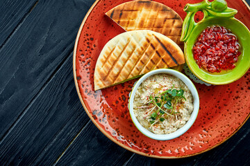 Traditional Israeli or oriental Baba ghanoush with vegetable salsa and pita, served in a red plate on a dark background. Eggplant restaurant dish