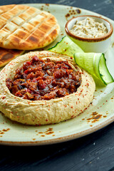 A classic oriental dish - chickpea hummus with baked vegetables and olive oil served with baked pita in a plate on a dark wood background. Vegetarian food. Diet
