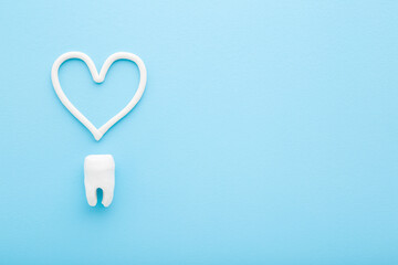 Heart shape created from toothpaste above white tooth on light blue table background. Pastel color. Closeup. Care about teeth. Empty place for text. Closeup. Top down view.