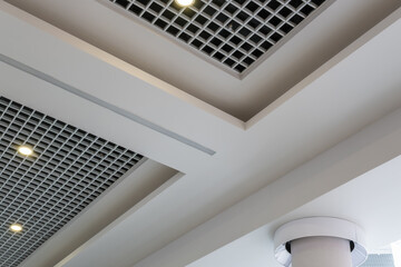 suspended and grid ceiling with halogen spots lamps and drywall construction in empty room in store or house. Stretch ceiling white and complex shape.