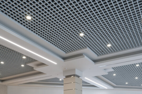 suspended and grid ceiling with halogen spots lamps and drywall construction in empty room in store or house. Stretch ceiling white and complex shape.