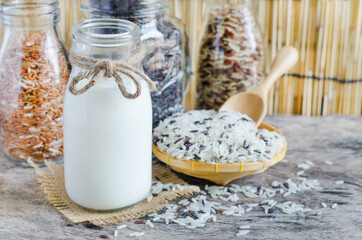 Closed up organic rice milk in glass bottle over blur variety rice seed on wooden background