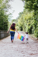 Young mother and little daughter walk while waving a rainbow flag, the symbol of the LGBT...
