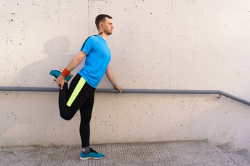 Young man runner getting ready to run stretching legs warm up quad stretch exercise on outdoor staircase