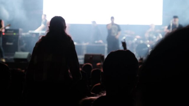 Crowd of people at a rock concert. Silhouettes lot of people dancing at an open-air music festival. Fans applaud, raise hands up and photographed, filmed concert on smartphones. Party People in Action