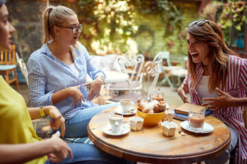 group of female friends talking in outdoor cafe, showing on their bellies, laughing.