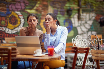 two young adult females sending kisses to someone online, looking at the laptop