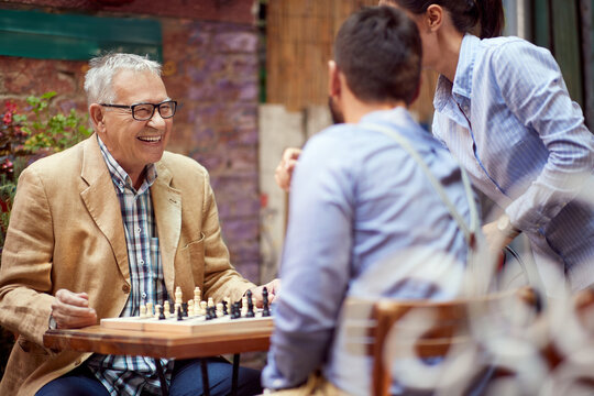 older caucasian male smiling, happy to win in chess game. sitting in outdoor cafe with his younger opponent.