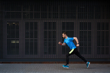 Fototapeta na wymiar Sport, fitness concept. Sporty man in a blue shirt running outdoors, spring running, attractive Caucasian runner jogs fast over urban gray background