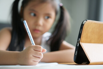 asian child student back to school or kid girl e-learning write note or draw by pencil and read on computer tablet with doing homework to think or people learn from home study online on smartphone pad