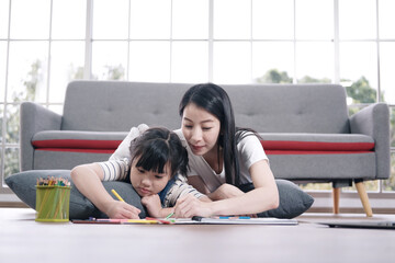 Smiling Asian mother and little asian girl child is drawing and Painting with wooden colored pencils on paper for imagination together in living room. Homeschool and educational concept