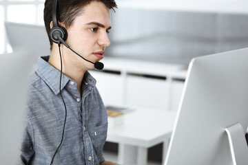 Casual dressed young man using headset and computer while talking with customers online. Call center, business concept