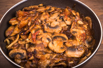 Stewed mushrooms champignons with tomato and garlic sauce on a plate on the table, close-up. Fried mushrooms