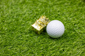 Golf ball with golden gift box on green grass