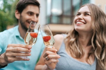 Happy couple portrait clinking two glasses with sparkling wine and strawberries inside with blurred...