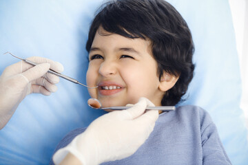 Cute arab boy sitting at dental chair with open mouth during oral checking up with doctor. Visiting dentist office. Stomatology concept