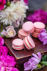 Pink macaroons lie on a wooden box surrounded by peony flowers