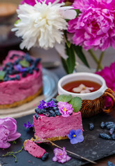 Obraz na płótnie Canvas piece of berry dessert lying next to a mug of tea, violet flowers and a background of peonies