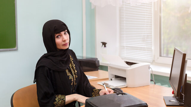 A Muslim teacher in national dress sits at desk in the office.