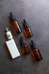 Vaping device e-cigarette electronic cigarette and liquid bottles on dark black stone shale...