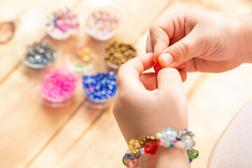 The child makes jewelry with his own hands, stringing colorful beads on a thread