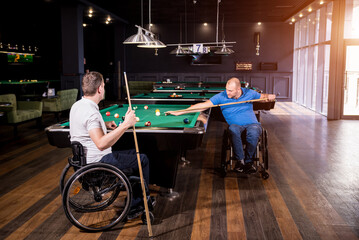 Adult men with disabilities in a wheelchair play billiards in the club
