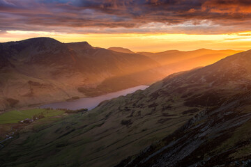 Spectacular Lake District sunset with beautiful glowing rays of light shining onto mountains and valley of Buttermere. Rugged British landscape with dramatic clouds in sky.