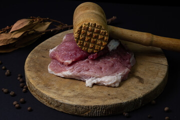 A kitchen hammer and a piece of meat next to it. Wooden kitchen hammer for meat. Meat on black...