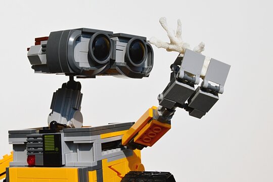 LEGO figure of Wall-E robot from Disney Pixar movie examining white sea coral in his left arm, light grey background.