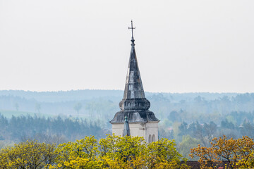 Wieża kościelna wśród kwitnących drzew. Symbol chrześcijaństwa - kościół z krzyżem - obrazy, fototapety, plakaty