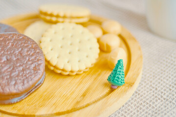 Cookies and cakes on a wooden tray. A small green Christmas tree made of plasticine. Chocolate sweets. The concept of Christmas and the New year. White cup on the background.