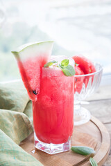 A watermalon smoothie in a glass , a piece of watermelon and green napking on a wooden cutting board.   