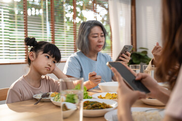 Upset daughter feel bore for addicted family use phone on lunch table.