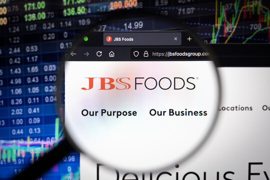 JBS company logo on a website with blurry stock market developments in the background, seen on a computer screen through a magnifying glass
