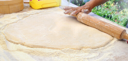Woman chef rolls out yeast dough with a rolling pin on the table. Copy space. Cooking outdoor. Master Class on making sweet donuts.
